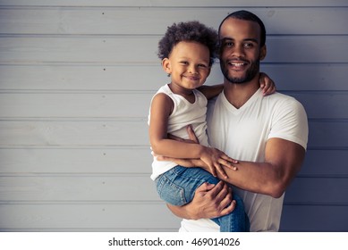 Portrait Of Handsome Young Afro American Father And His Cute Child Hugging, Looking At Camera And Smiling