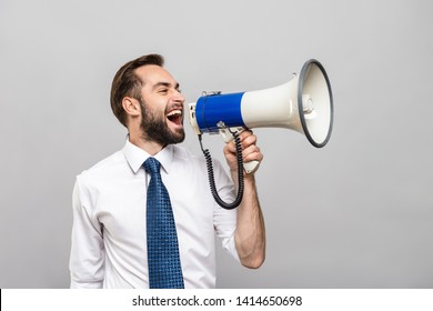 Portrait of a handsome young businessman wearing white shirt and tie standing isolated over gray background, holding loudspeaker, screaming
