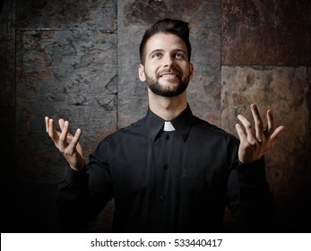 Retrato de un hermoso joven sacerdote católico que predica mirando hacia arriba sonriendo.