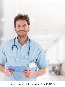 Portrait Of Handsome Young Doctor On Hospital Corridor Looking At Camera, Smiling.?