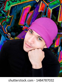 Portrait of a handsome young with green eyes wearing a pink woolen cap and smiling in front of a graffiti wall