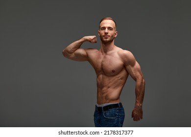 Portrait of a handsome young guy model a shirtless with a muscular healthy body, showing off his biceps muscles on a gray background