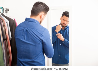 Portrait Of A Handsome Young Hispanic Man Getting Dressed On Casual Clothes In Front Of A Mirror