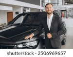 Portrait of a handsome young male car salesman working on the showroom floor. Happy salesperson standing in a car showroom