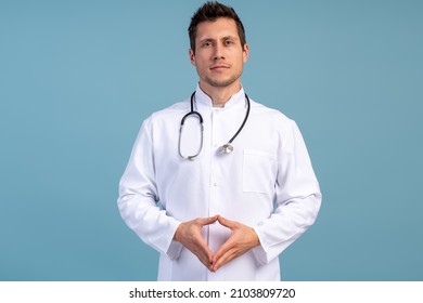 Portrait of handsome young male doctor in white medical jacket isolated on blue background. Brunette man surgeon smiling at the camera 