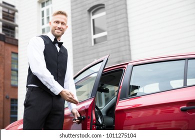 Portrait Of A Handsome Young Male Valet Opening Red Car Door