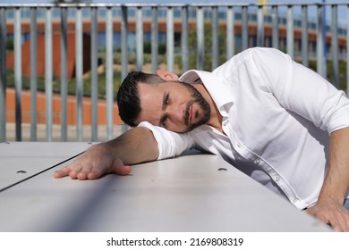 Portrait of handsome young man, with blue eyes, beard and white shirt, with his head resting on a white wooden table, sad and worried. Concept beauty, depression, worry, thoughts, sadness.