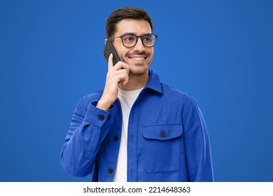 Portrait of handsome young man in blue shirt and glasses, answering phone call, looking aside with smile, isolated on blue background - Powered by Shutterstock