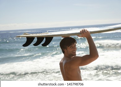 Portrait of handsome young man carrying surfboard by ocean - Powered by Shutterstock