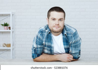 Portrait of handsome young man in casual shirt keeping arms crossed looking at the camera while sitting against a wall in an home. - Shutterstock ID 523881076