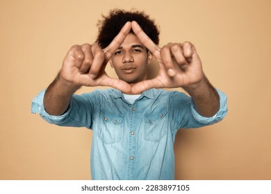 Portrait of handsome young man with dark skin and afro hair in blue denim shirt making and showing triangle gesture on brown background. Environment protection, recycling and reusing concept - Shutterstock ID 2283897105