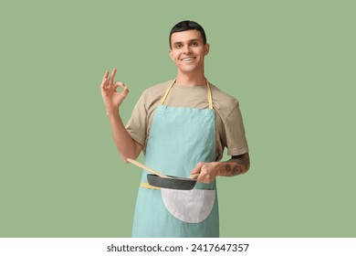 Portrait of handsome young man with frying pan showing OK on green background - Powered by Shutterstock