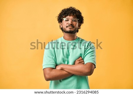Portrait of a handsome young man in glasses and a turquoise t-shirt with his arms crossed looking at the camera.