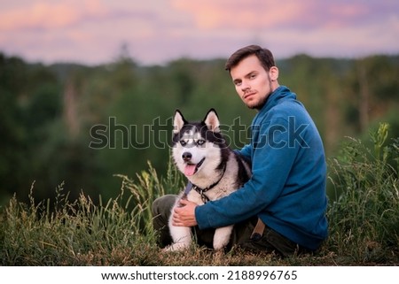 Portrait of handsome young man and his pet dog Siberian Husky in nature.