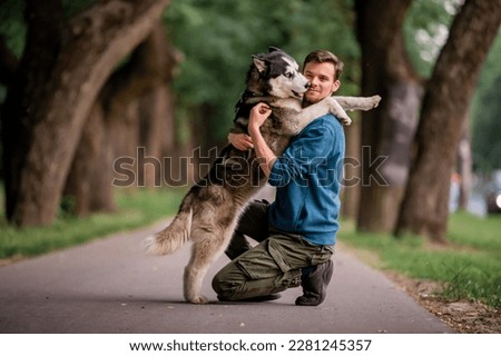 Portrait of handsome young man and his beloved dog Siberian Husky hugging in nature.