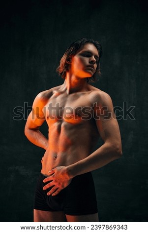 Portrait of handsome young man with muscular beautiful shirtless body posing against dark textured studio background. Concept of men's beauty, health, body art and aesthetics, care, sportive lifestyle