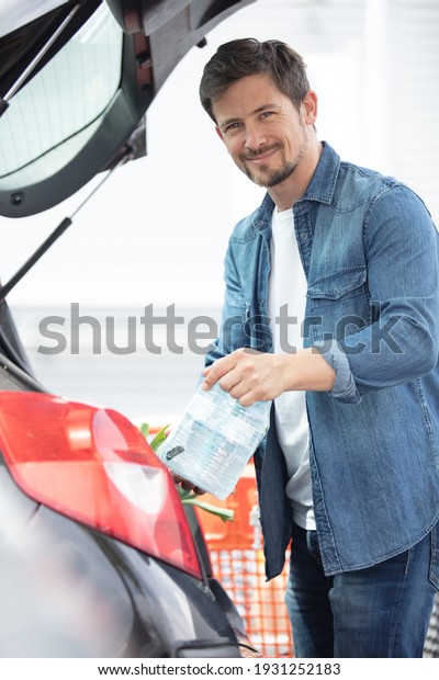 portrait of handsome young man packing groceries\
into car trunk
