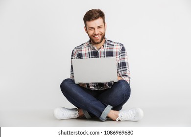 Portrait of a handsome young man in plaid shirt sitting on a floor with laptop computer isolated over white background - Shutterstock ID 1086969680