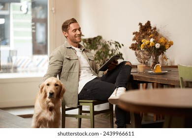 Portrait of handsome young man sits in cafe with his dog, petting golden retriever, reading news on tablet, relaxing with cup of coffee. - Powered by Shutterstock