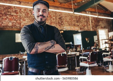 Portrait Of Handsome Young Man Standing At Barber Shop. Stylish Hairstylist Standing In His Salon With His Arms Crossed.