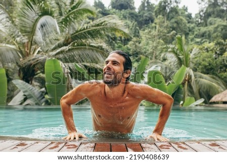 Portrait of handsome young man in swimming pool. Caucasian man in pool looking away and smiling. Male at luxury holiday resort.