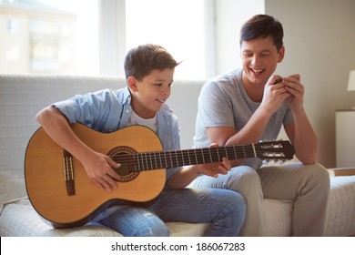 Portrait of handsome young man teaching his son how to play the guitar - Powered by Shutterstock