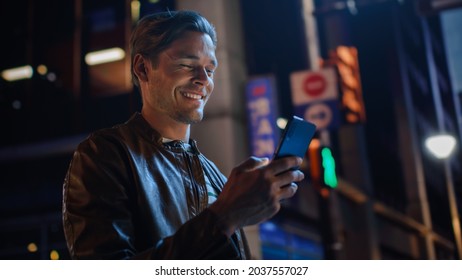 Portrait of Handsome Young Man Using Smartphone Standing in the Night City Street Full of Neon Lights. Smiling Stylish Blonde Male Using Mobile Phone for Social Media Posting. - Powered by Shutterstock