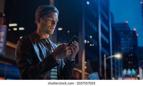 Portrait of Handsome Young Man Using Smartphone Standing in the Night City Street Full of Neon Lights. Smiling Stylish Blonde Male Using Mobile Phone for Social Media Posting. - Powered by Shutterstock