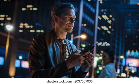 Portrait of Handsome Young Man Using Smartphone Standing in the Night City Street Full of Neon Lights. Smiling Stylish Blonde Male Using Mobile Phone for Social Media Posting. Dutch Angle Shot. - Shutterstock ID 2037557036