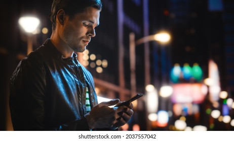 Portrait of Handsome Young Man Using Smartphone Standing in the Night City Street Full of Neon Lights. Smiling Stylish Blonde Male Using Mobile Phone for Social Media Posting. - Powered by Shutterstock