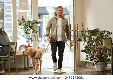 Portrait of handsome young man walks into the cafe with his dog on a leash, enters pet-friendly coffee shop, opens the door.