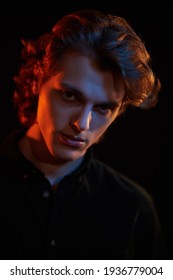 Portrait of a handsome young man with wavy hair  in mixed color light on a black background. Men's beauty. Copy space.