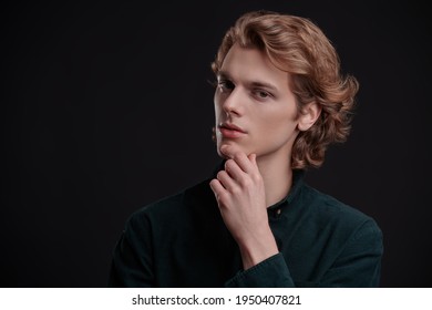 Portrait of a handsome young man with wavy blond hair posing on a black background. Men's beauty. 