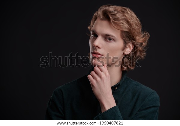 Portrait of a handsome young\
man with wavy blond hair posing on a black background. Men\'s\
beauty. 