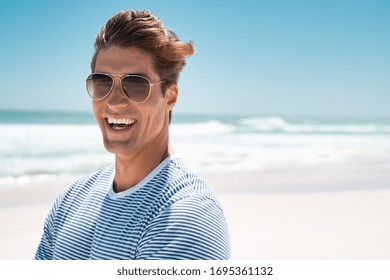 Portrait Of Handsome Young Man Wearing Sunglasses And Looking At Camera. Portrait Of Joyful Man Enjoying Summer Holiday At Beach. Young Casual Man In Shades With Big Grin And Copy Space.