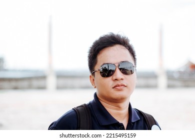 Portrait Of Handsome Young Man Wearing Sunglasses And Looking At Camera. Portrait Of Joyful Man Enjoying Summer Holiday At Beach. Young Casual Man In Shades With Big Grin And Copy Space