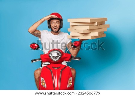 Portrait of a handsome young man in a white t-shirt and red helmet riding a red scooter with pizza boxes on his head.