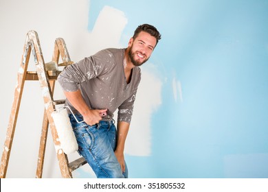 Portrait of handsome young painter in paint splattered shirt painting a wall with paint roller and leaning on a wooden ladder - Powered by Shutterstock