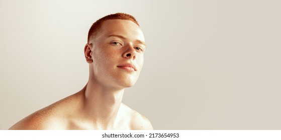 Portrait of handsome young red-haired man with freckles posing, barely smiling, looking at camera isolated over grey studio background. Concept of men's health, lifestyle, beauty, body and skin care - Powered by Shutterstock