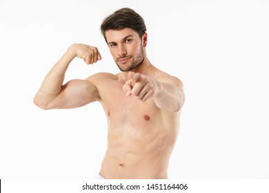 Portrait of a handsome young shirtless sportsman standing isolated over white background, flexing biceps, pointing finger at camera