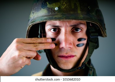 Portrait of handsome young soldier wearing a military uniform, painted his face with two fingers, in a gray background - Powered by Shutterstock