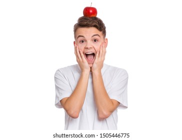 Portrait of handsome young teen boy balancing an red apple on his head, isolated on white background. Happy surprised child with raw vegetables and fruits. Organic natural healthy food produce.
