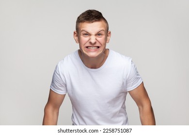 Portrait of handsome young teenager boy wearing T-shirt expressing aggressive emotions, screaming with hate and anger, frowning face. Indoor studio shot isolated on gray background. - Shutterstock ID 2258751087