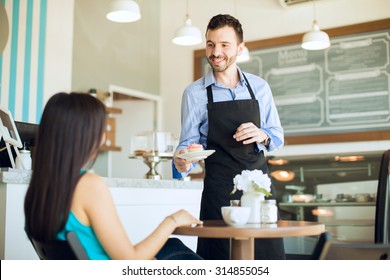 Portrait of a handsome young waiter serving some coffee and a cupcake to a female customer in a cafe - Powered by Shutterstock