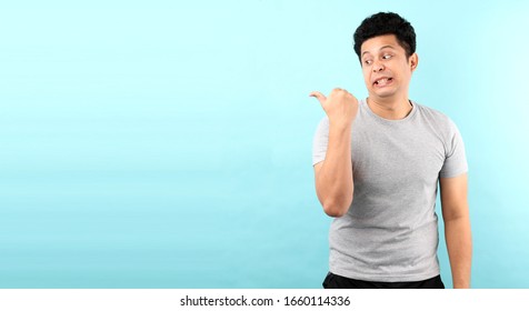 Portrait Of Handsome,Shock And Surprise Face Of Asian Man Pointing Finger  On Empty Space  Isolated On Blue  Background In Studio With Copy Space.