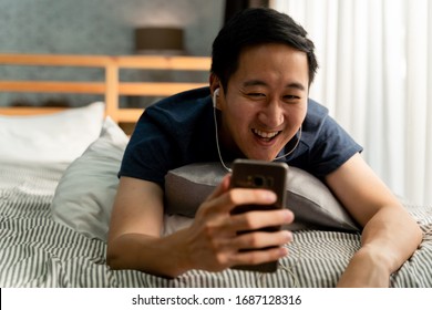 Portrait Of Happy 30s Aged Asian Man In Casual Clothing Making Facetime Video Calling With Smartphone At Home. Using Conferencing Meeting Online App, Social Distancing, Work From Home Concept