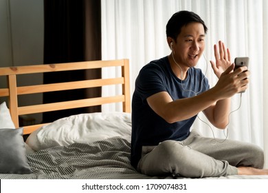 Portrait Of Happy 30s Aged Asian Man Making Facetime Video Calling With Smartphone At Home. He's Waving On Phone Screen. Using Conferencing Meeting Online App, Social Distancing, Concept