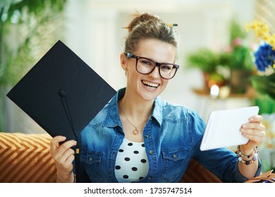 Portrait Of Happy 40 Years Old Woman In Jeans Shirt With Graduation Cap And Tablet PC At Modern Home In Sunny Day.