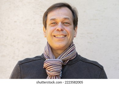 Portrait Of A Happy 45-50 Year Old Man In A Cardigan And Scarf On A Light Background, Close-up.