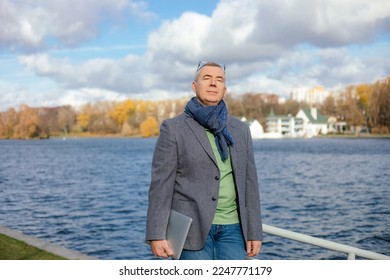 Portrait of happy 50 years old businessman in stylish clothes enjoying with closed eyes natural beauty. Man walk outdoors near water pond. Urban lifestyle, autumn nature, beautiful waterscape. - Shutterstock ID 2247771179
